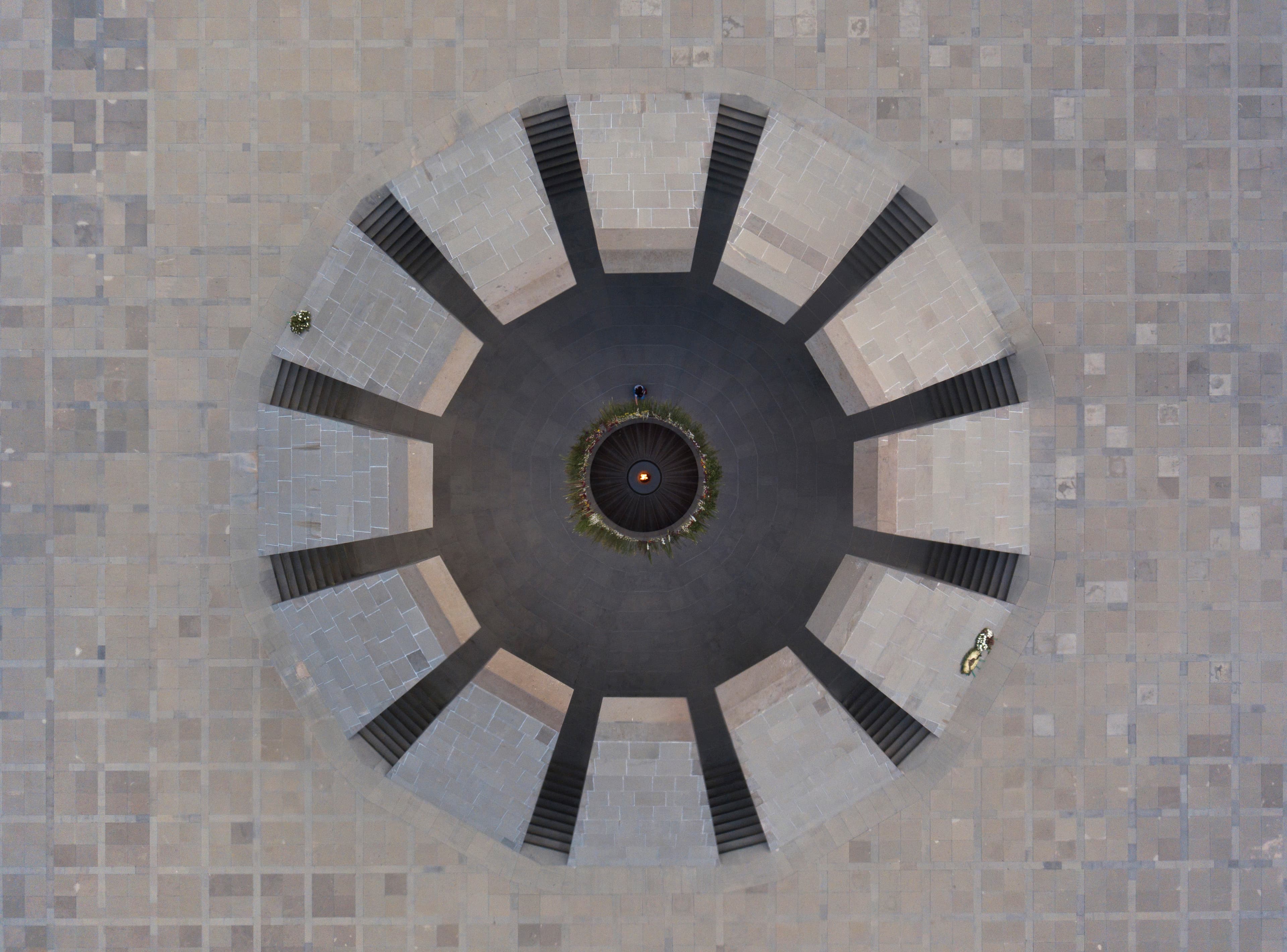 Aerial view: a girl lays a flower on the ring around the eternal flame at Tsitsernakaberd.