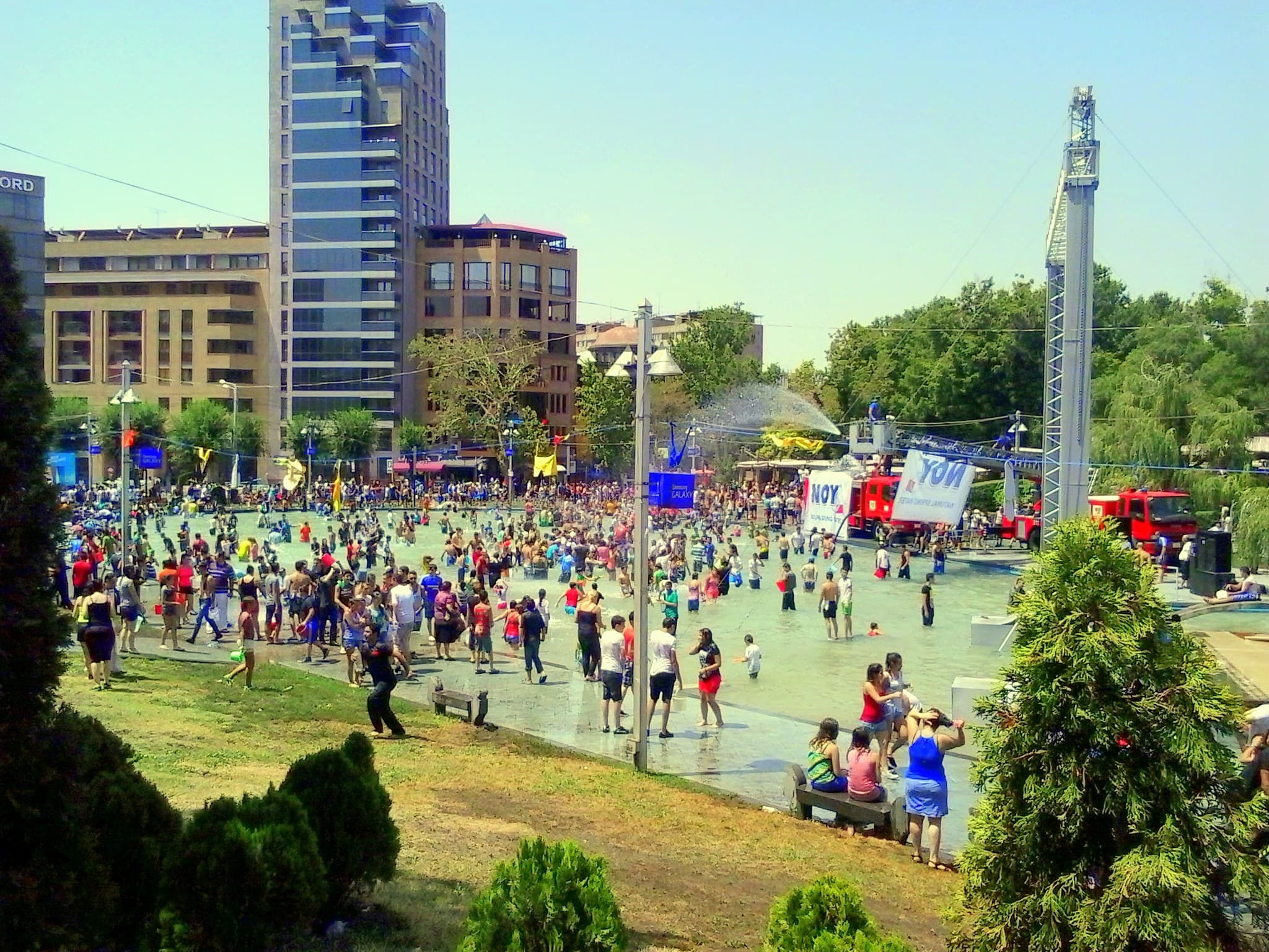 A huge crowd wading and splashing in a water-filled plaza during Vardavar in Yerevan.