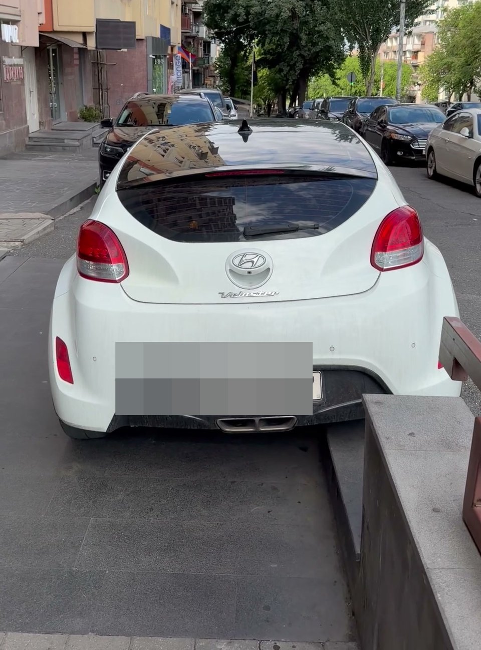 A car with its wheels mounted on a tiled sidewalk, rear plate visible